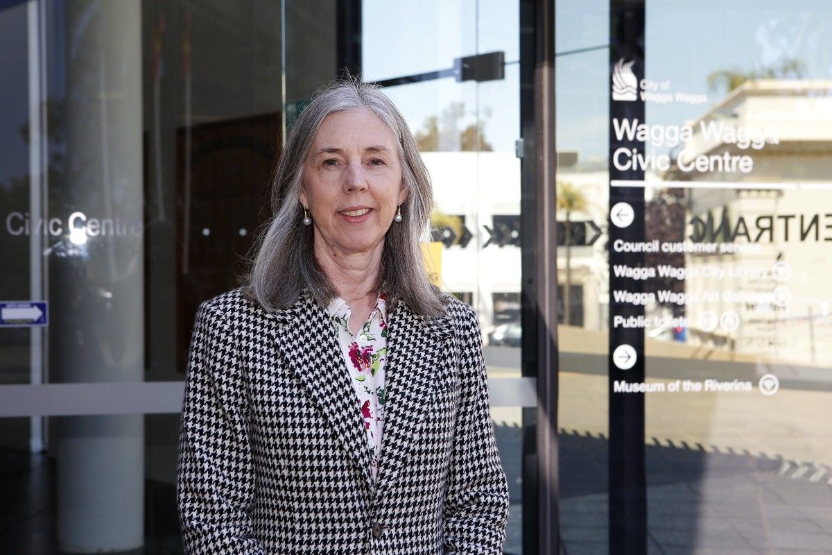 Woman wearing a houndstooth pattern coat, standing outside the front entrance to the Wagga Wagga Civic Centre building.