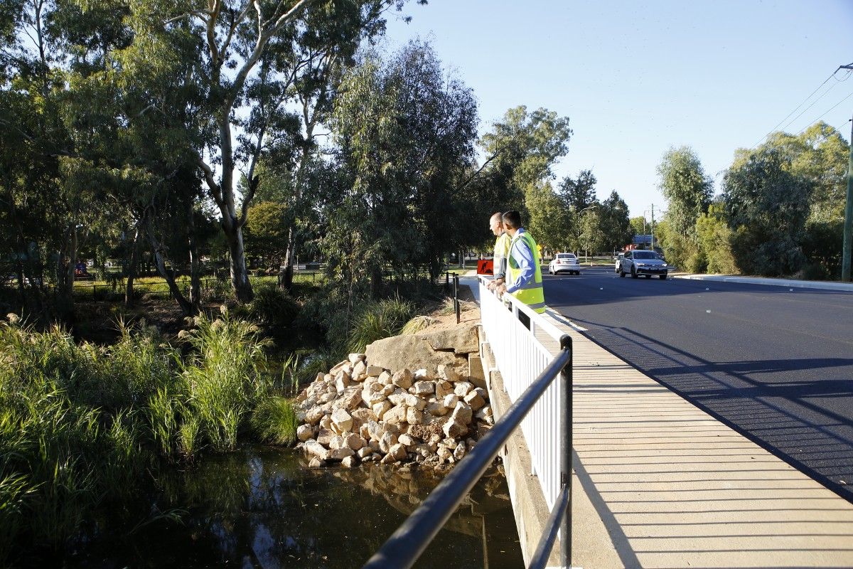 Two men in hi-vis shirts standing near railing of bridge.