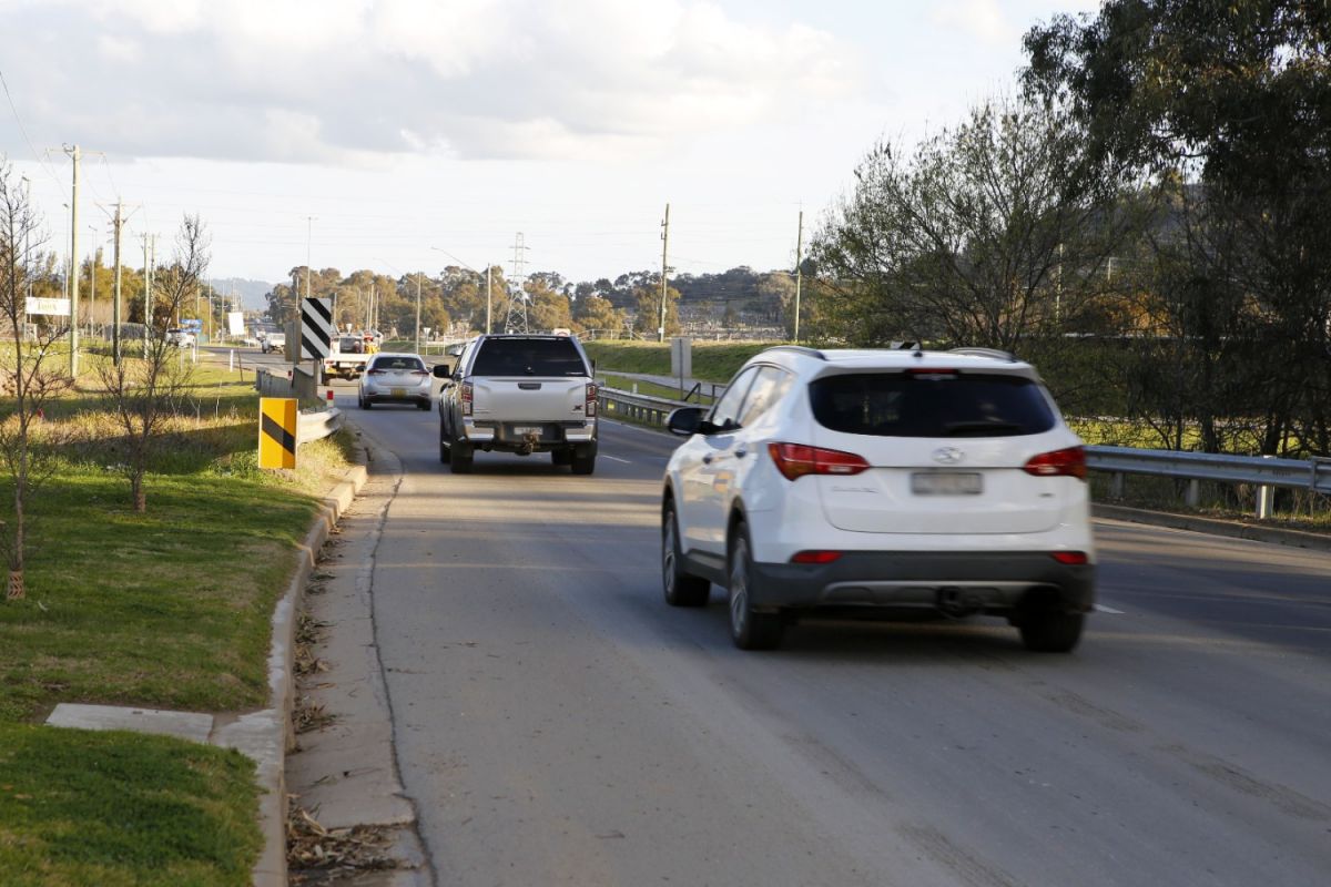 Cars and SUVs driving along a road crossing a narrow bridge.