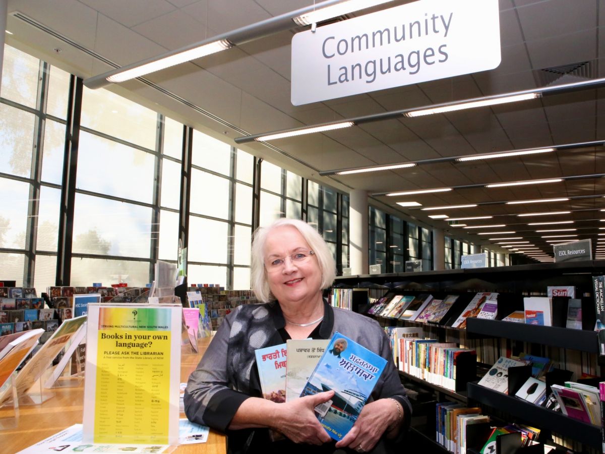 Woman holding books in Punjabi standing between library shelves, 