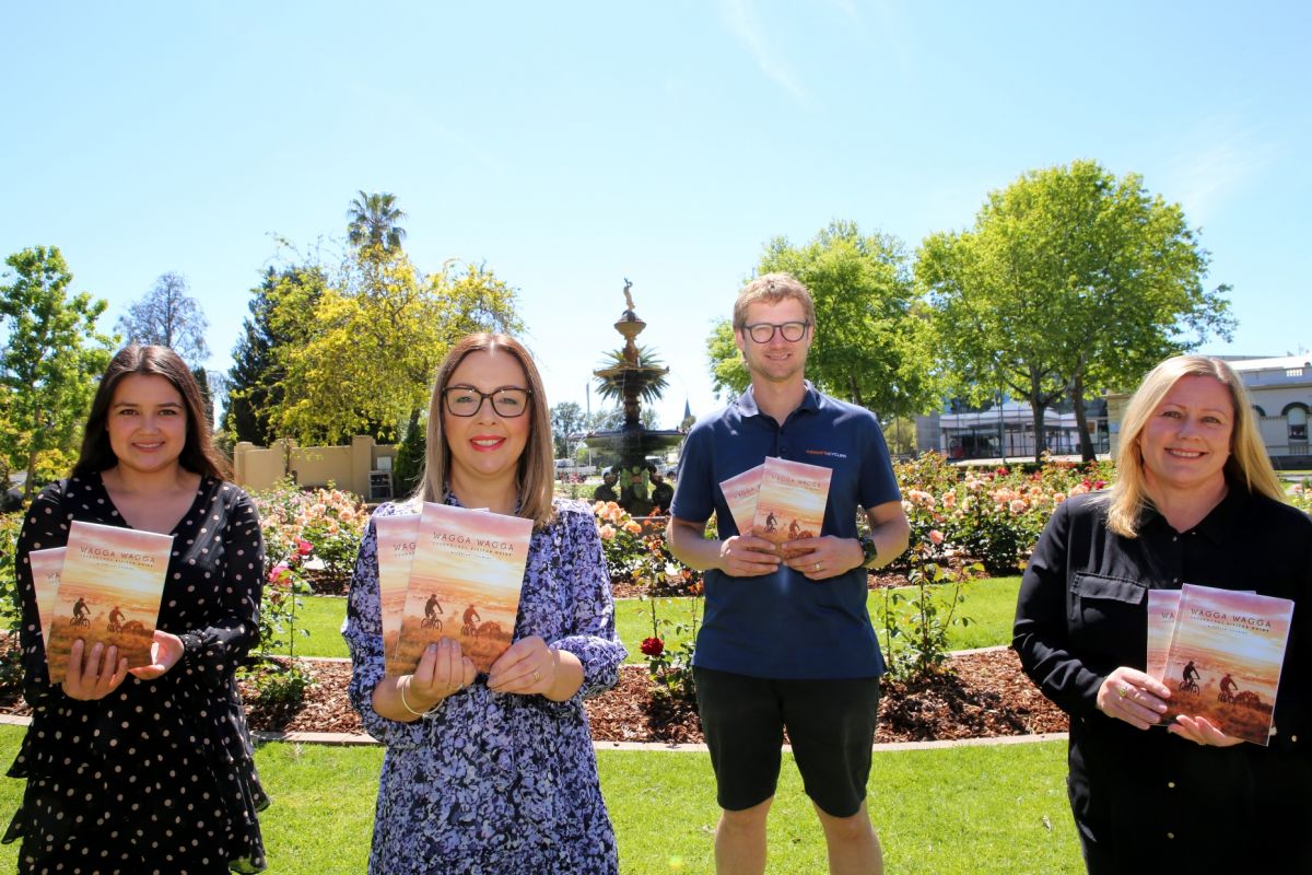 Two woman and two men holding copies of magazine, standing in front of fountain