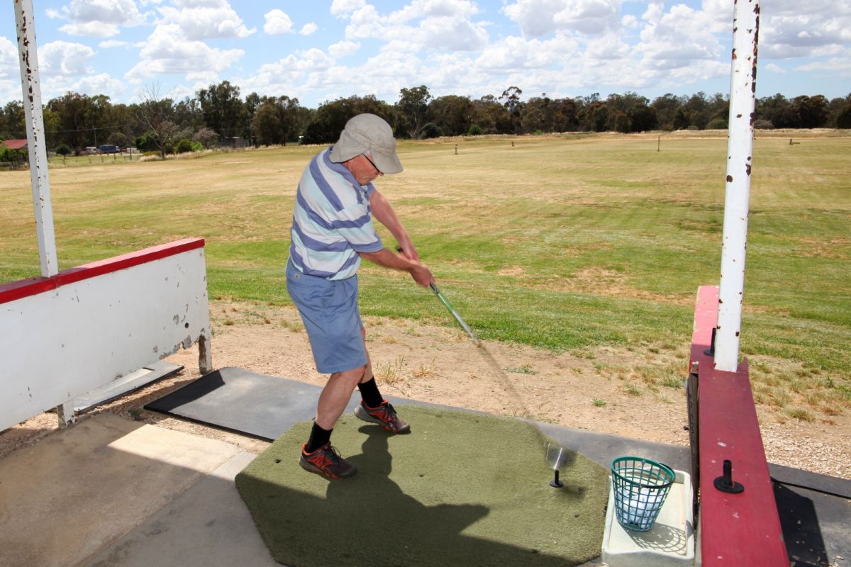 Male golfer teeing off under covered driving range