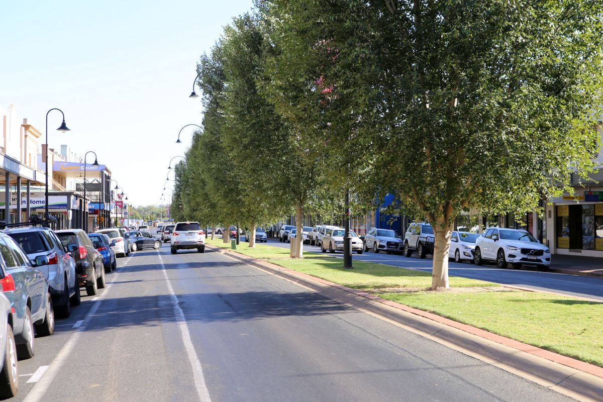 main street with trees on either side and cars parked and driving on street