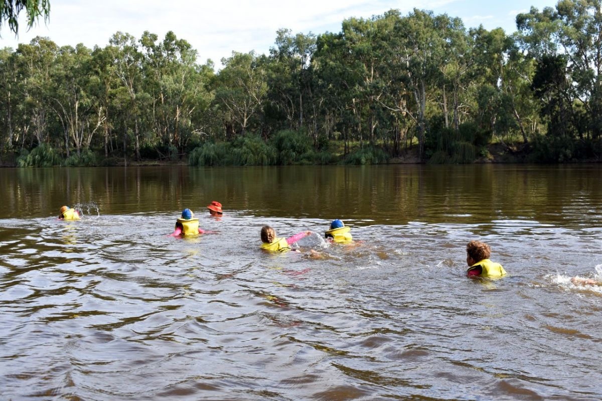 Children swim in the river with a swimming teacher