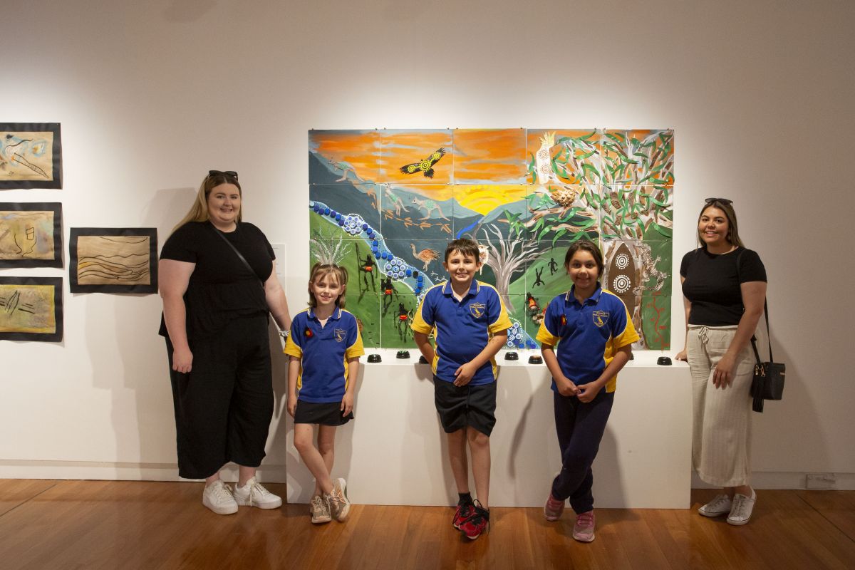 Two women and three children stand in front of a large artwork