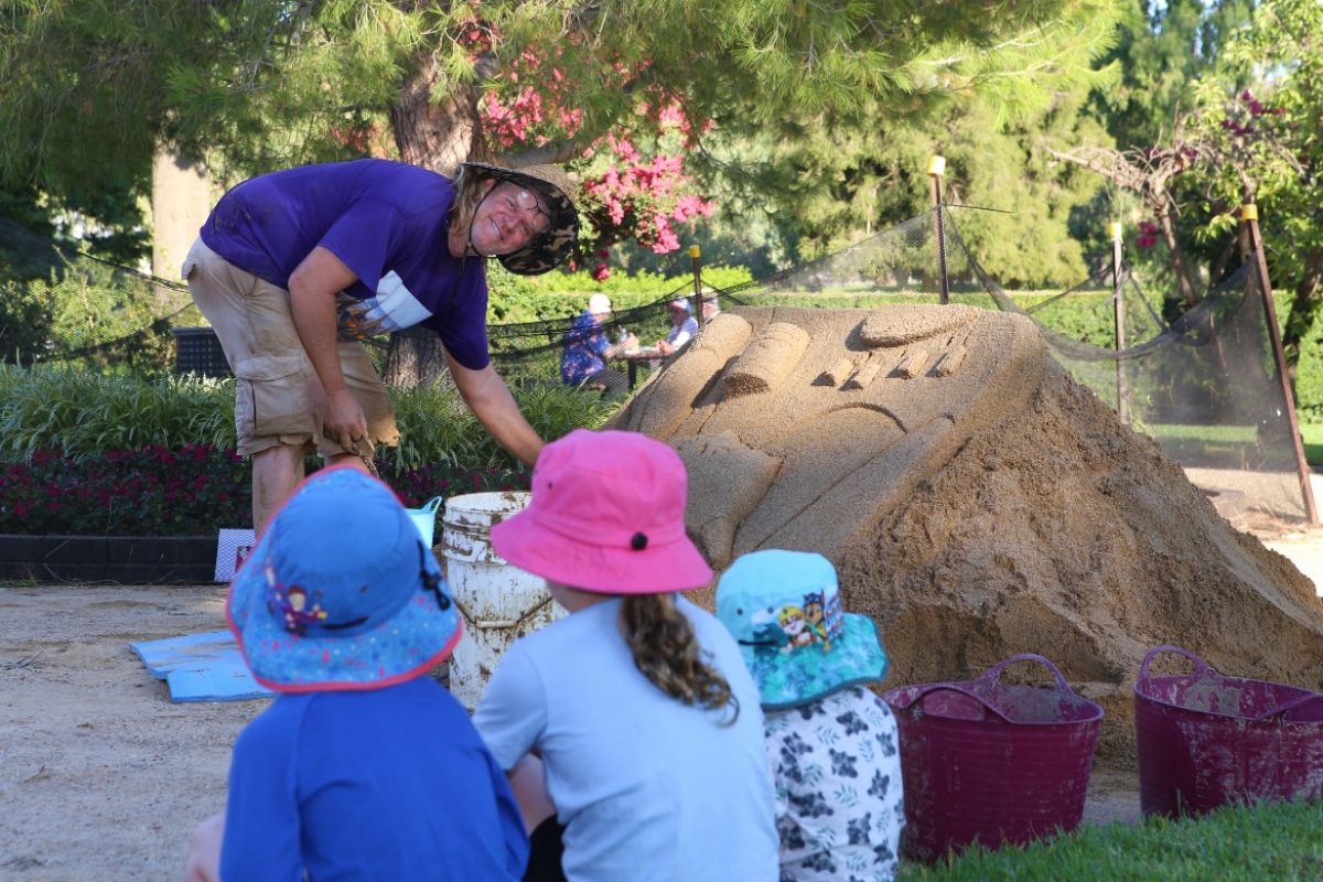 Back view of three children watching man build sandcastle