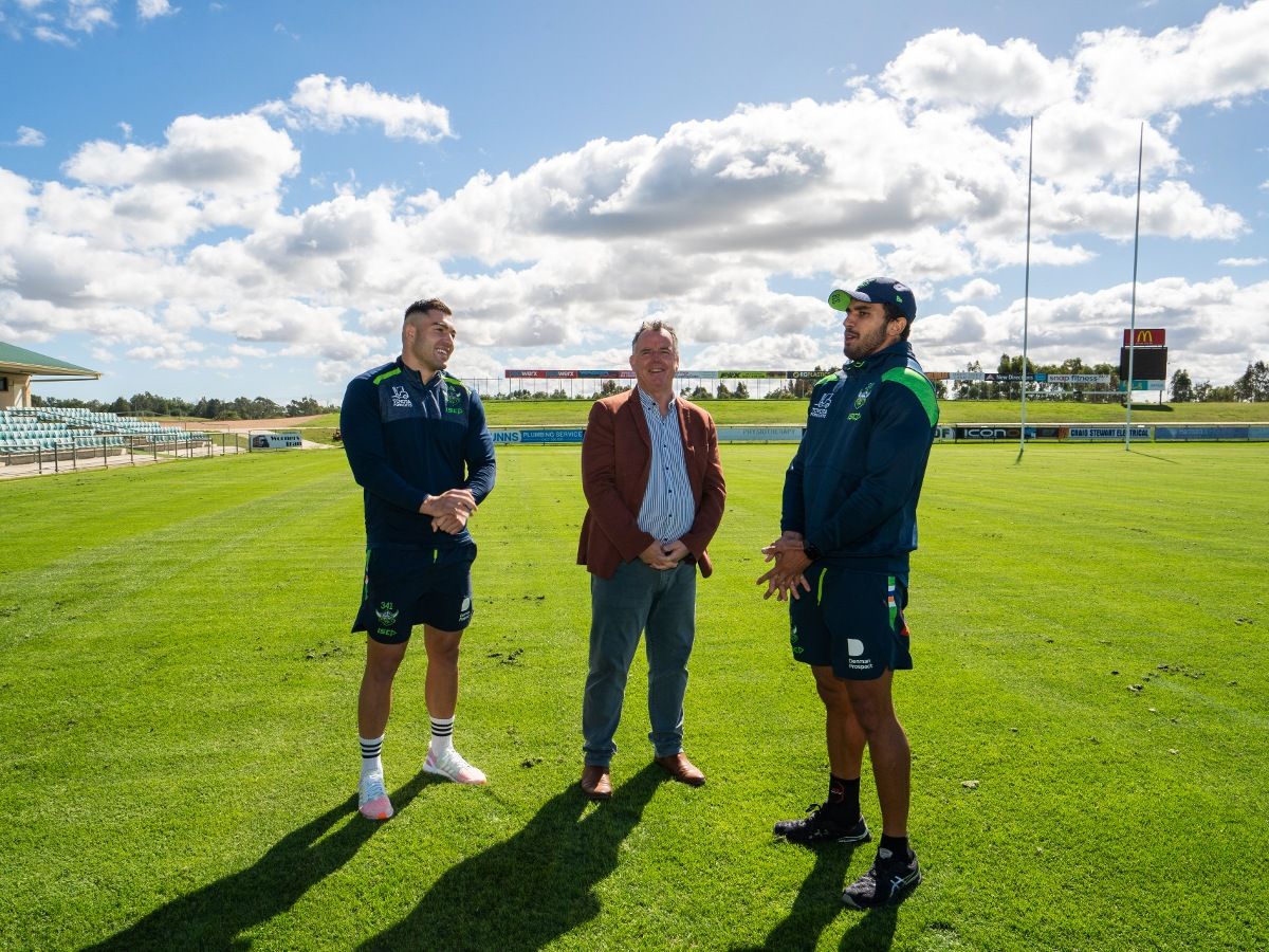 Two Raiders football players and Wagga mayor standing on football field