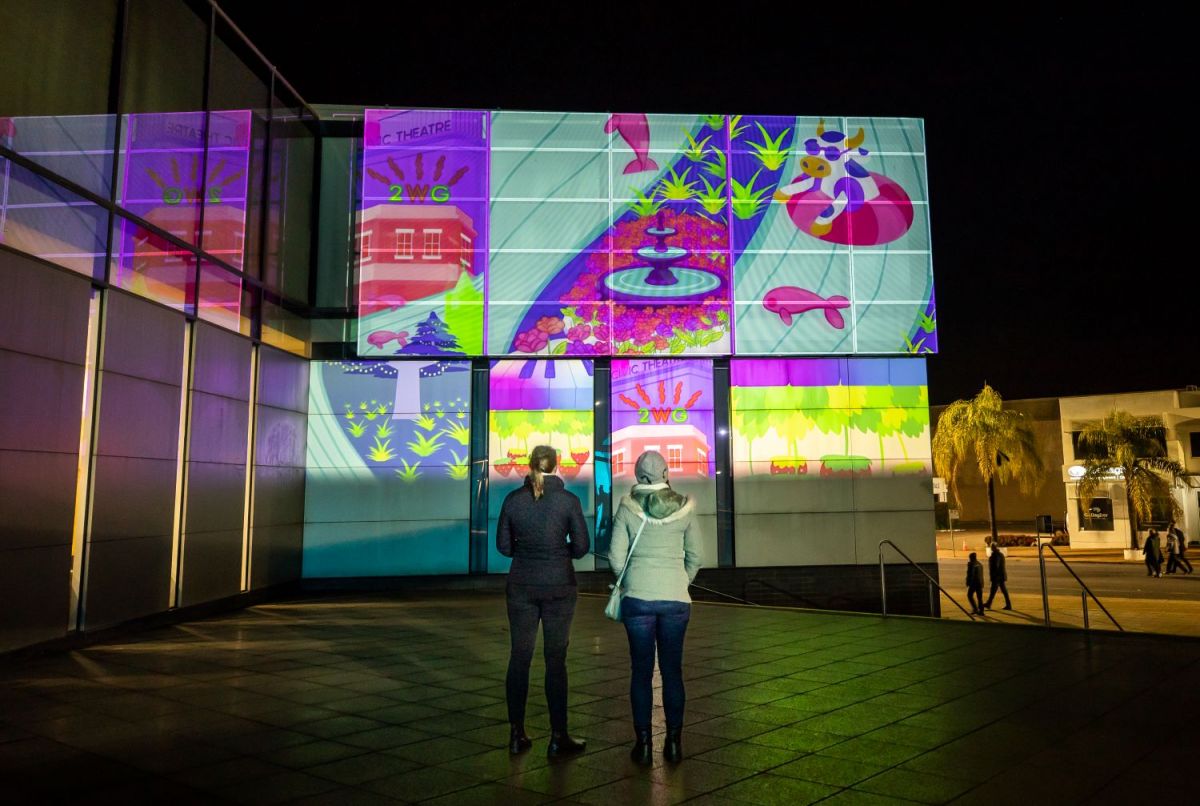 Two women standing in front of a projected artwork on the side of a building. 