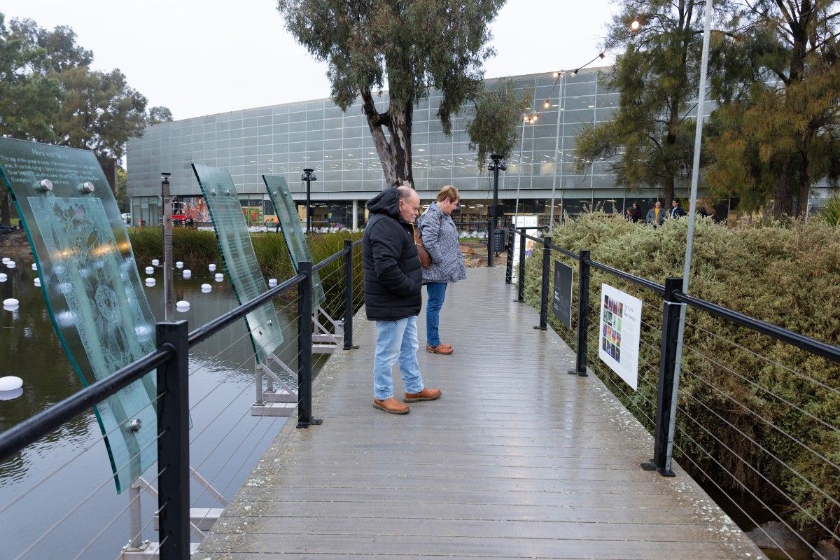 Man and woman standing on Wollundry Lagoon boardwalk reading sign with information about Many Dances soundscape installation