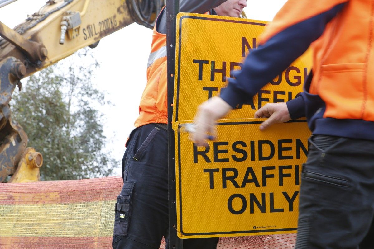 Close-up of arms and hands of two men removing sign which says Residents Traffic Only