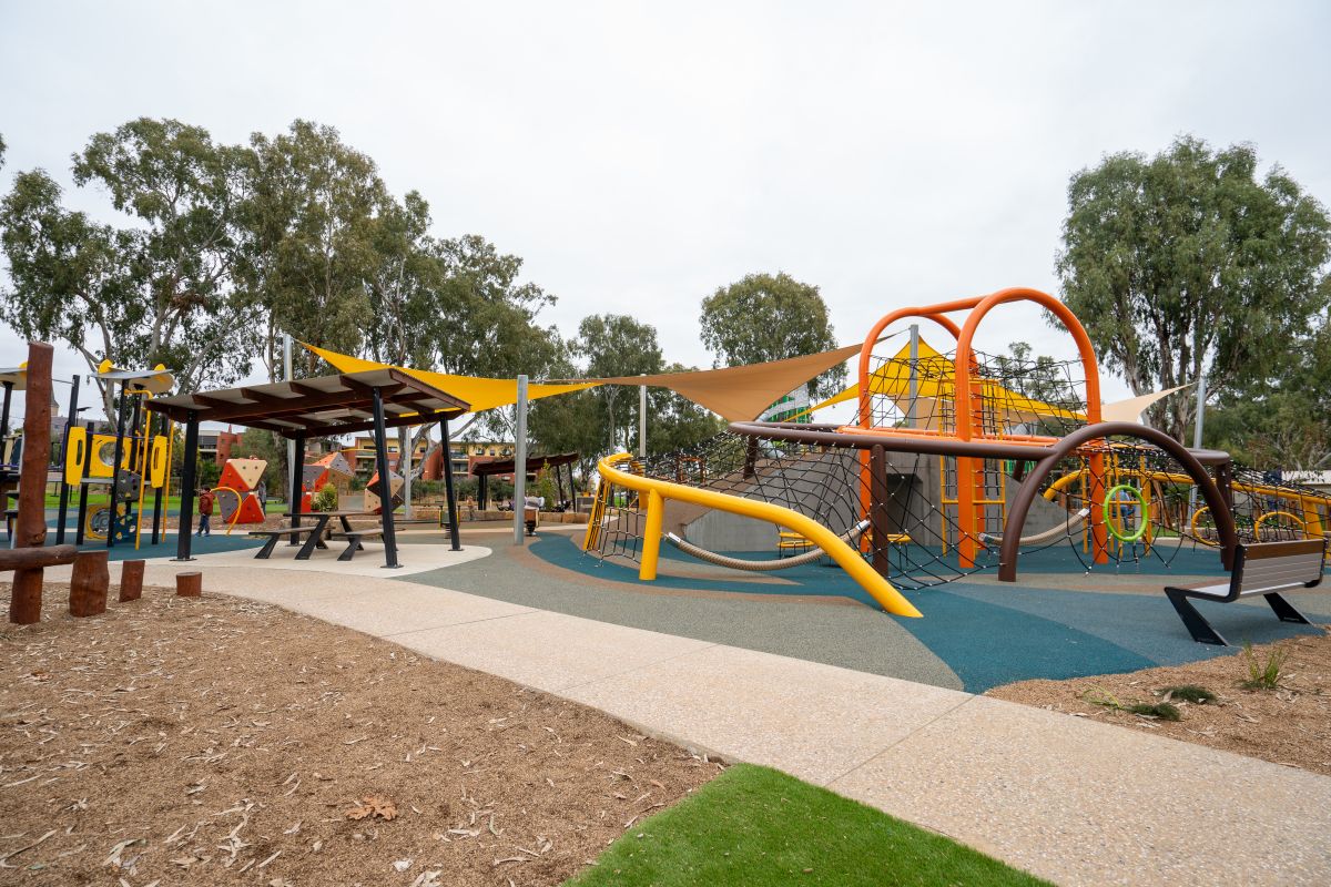 A large children's playground with orange, yellow and brown equipment. 