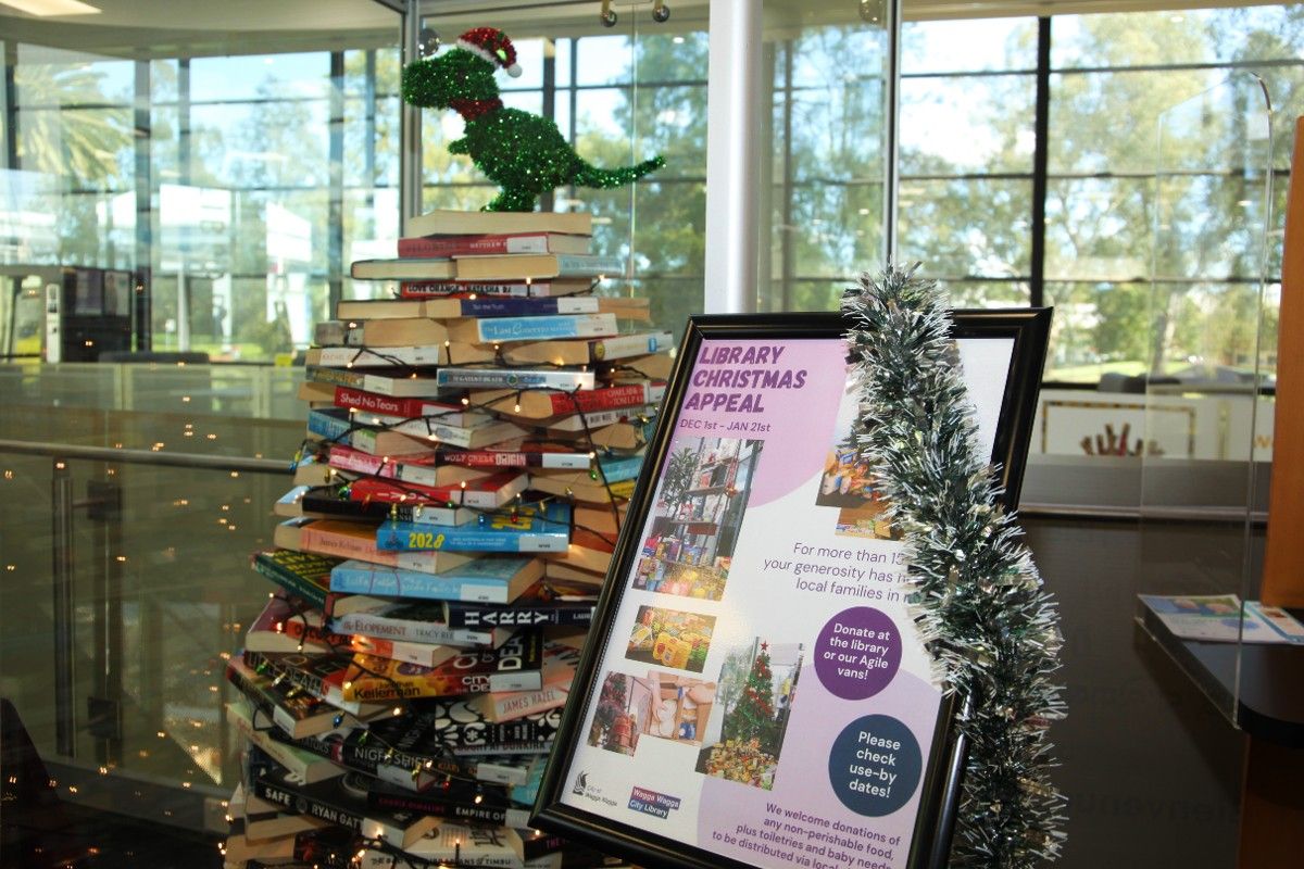 Sign with Library Christmas Appeal beside glass cabinet with Christmas tree created from books
