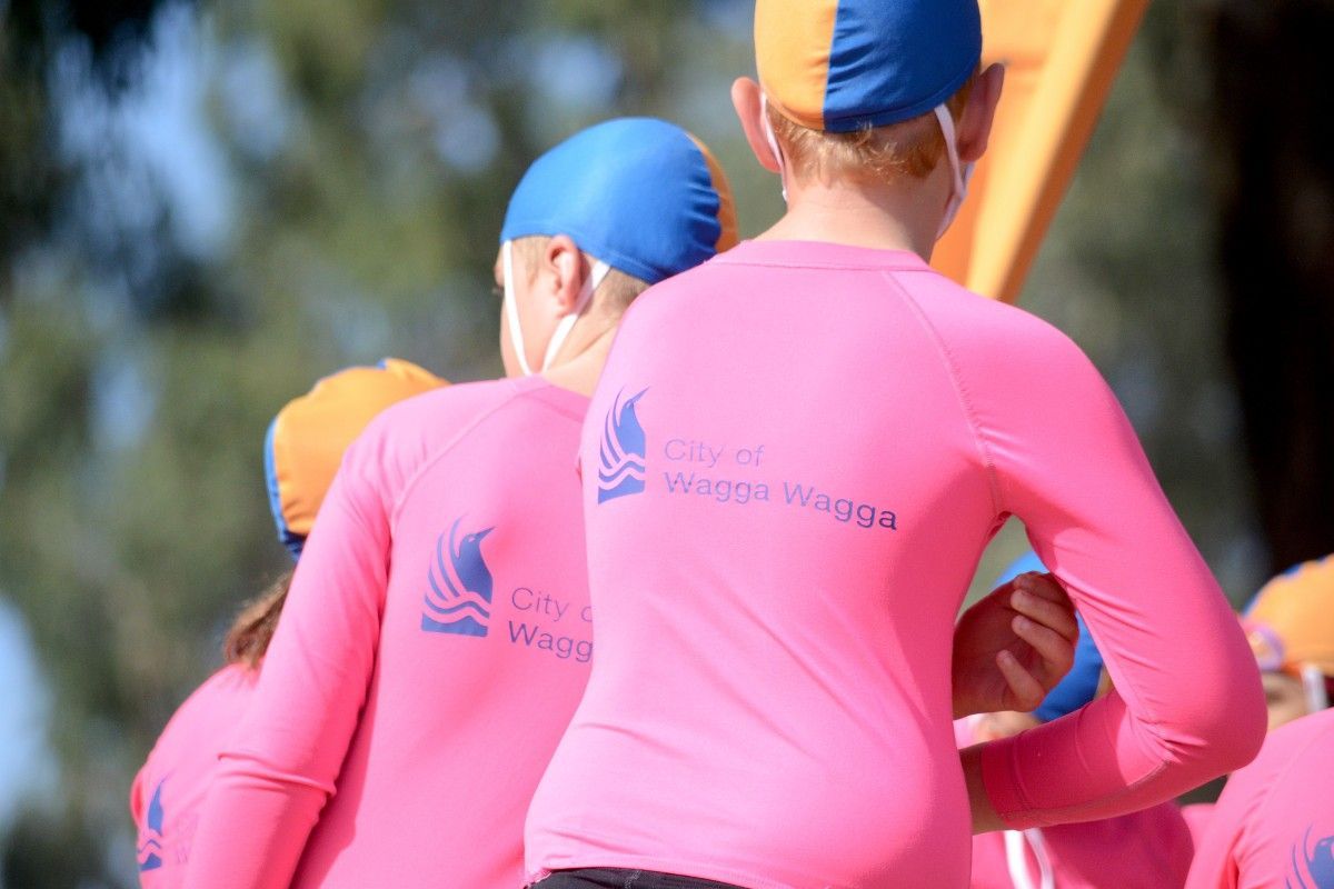 Back view of three young males wearing pink lifesaving tops and caps