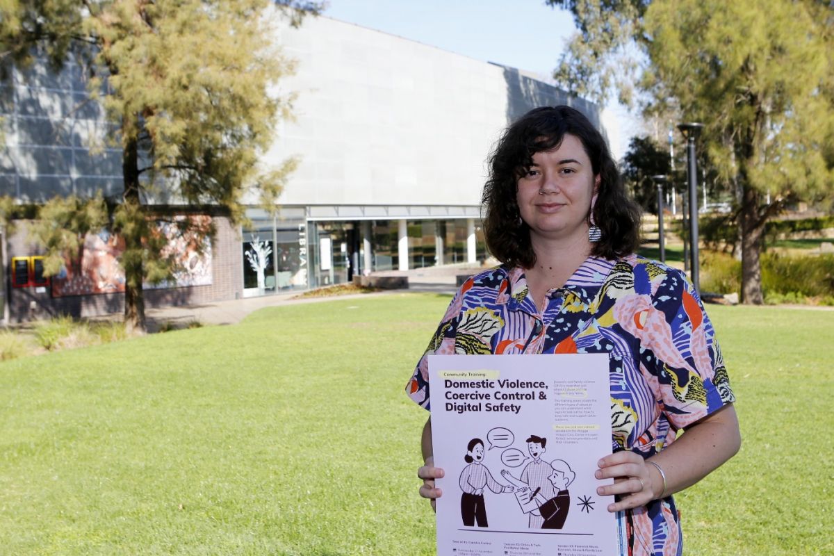 A woman holding a poster about domestic and family violence, coercive control, and digital safety.