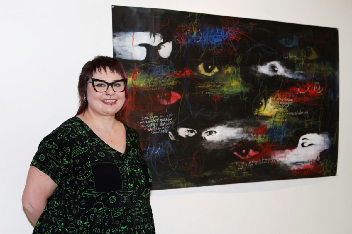 Artist stands in front of artwork displayed on wall.