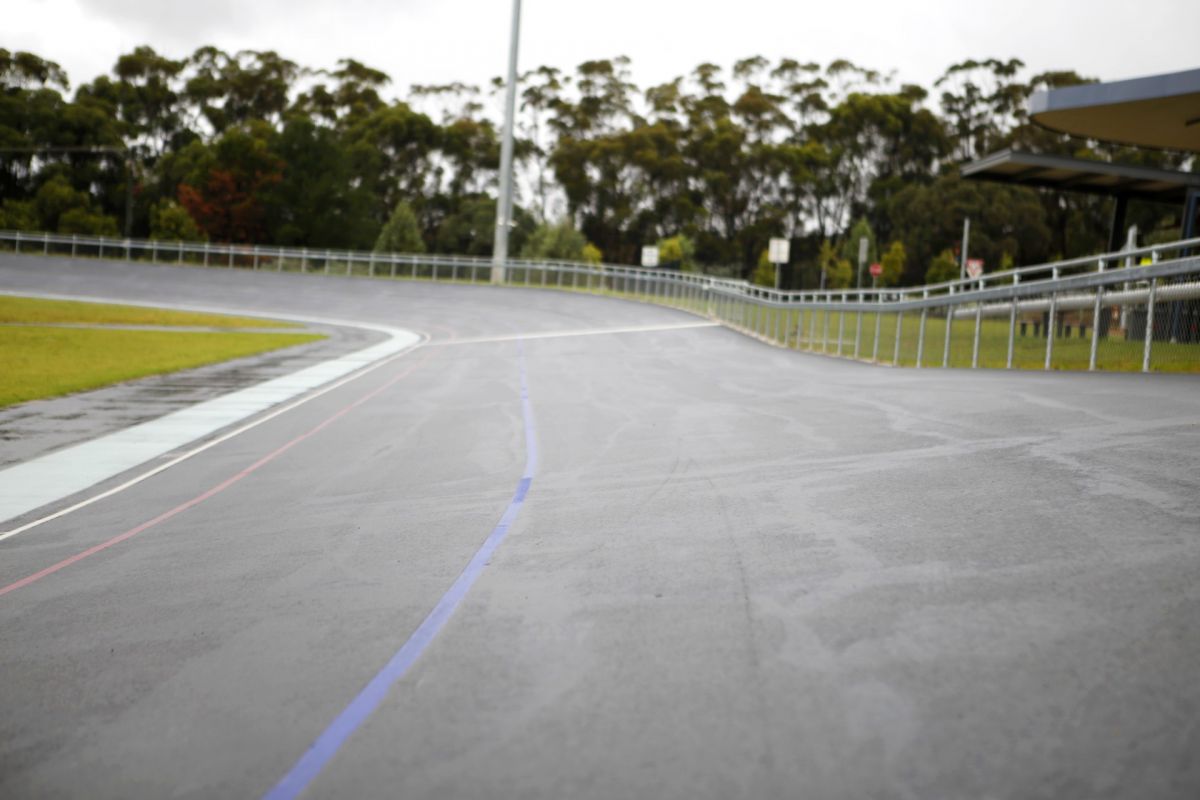 One side of an asphalt velodrome track, with fencing down the right-hand side.