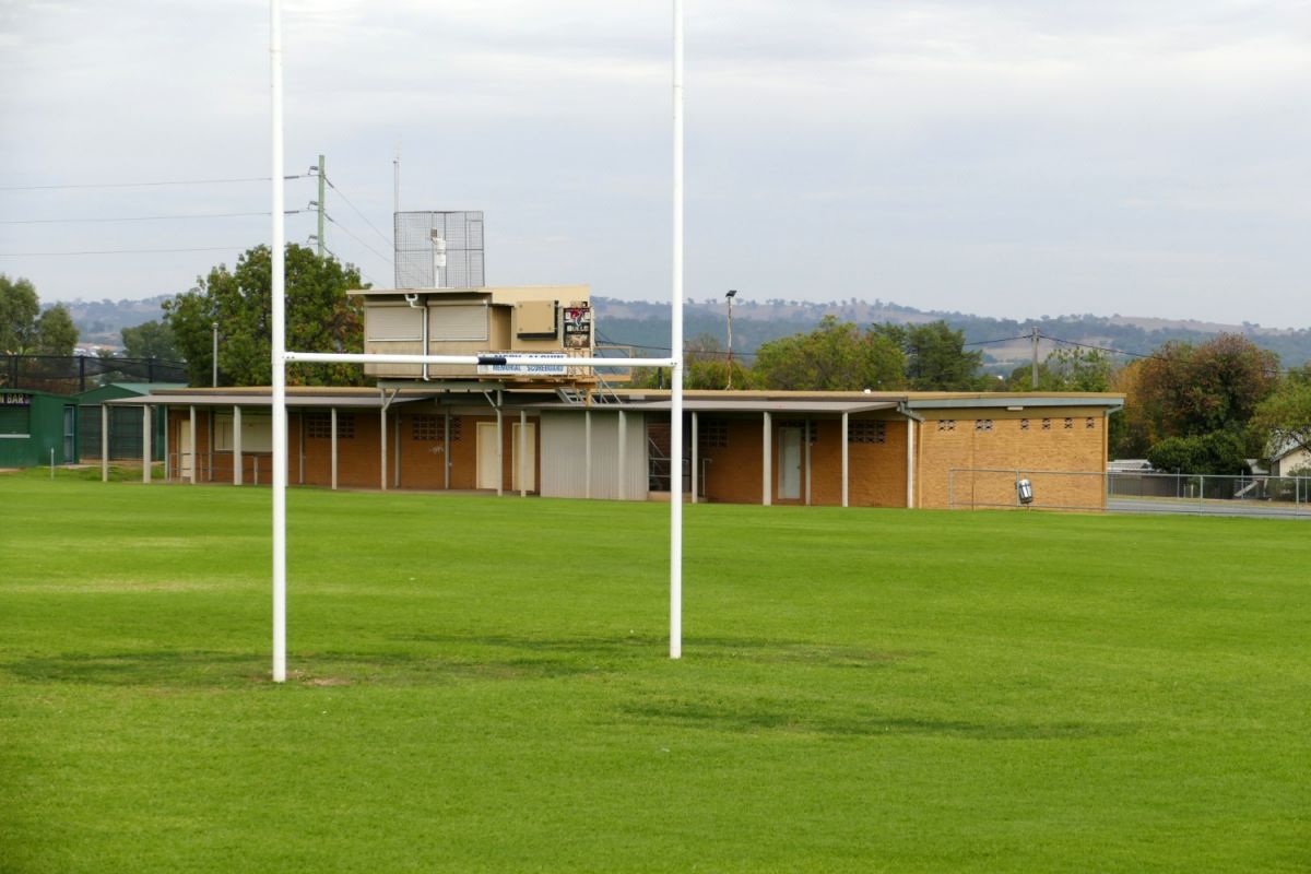 Rugby league goal posts and field in the foreground with brick amenities building in the background