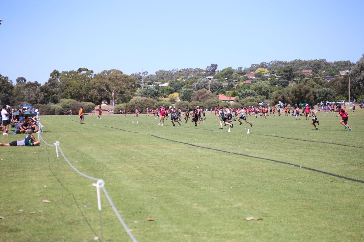 Junior male touch football players playing game on grass field, with people watching from sidelines