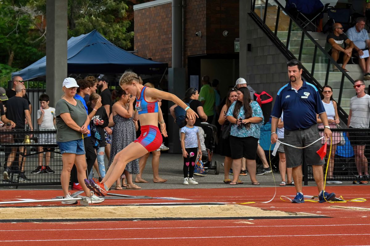 Side view of young female athlete landing in long jump