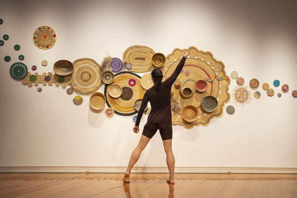 A woman dances in front of a woven artwork