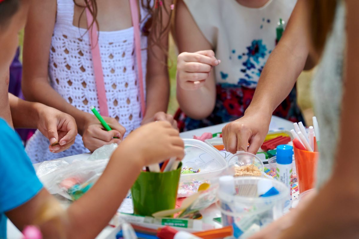 A group of children playing with craft materials such as paper, paint and glue. You can only see the children's torsos and arms. 
