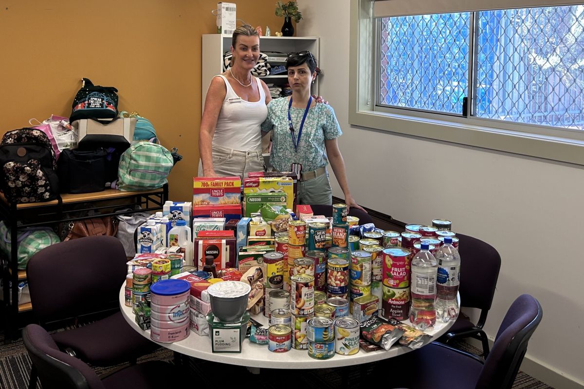 Tolland Community Centre Coordinator Stacey Prigg and Library Programs Officer Leila Davandeh stand at a table that is completely covered in donations of food and toiletries. 