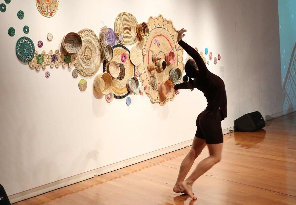 A woman dances in front of a woven artwork
