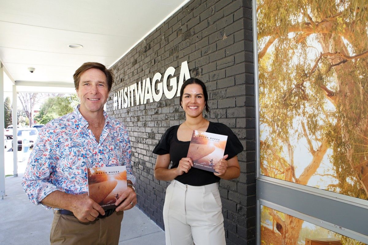 Man and woman standing in front of the #vistwagga sign on the exterior wall of the Visitor Information Centre