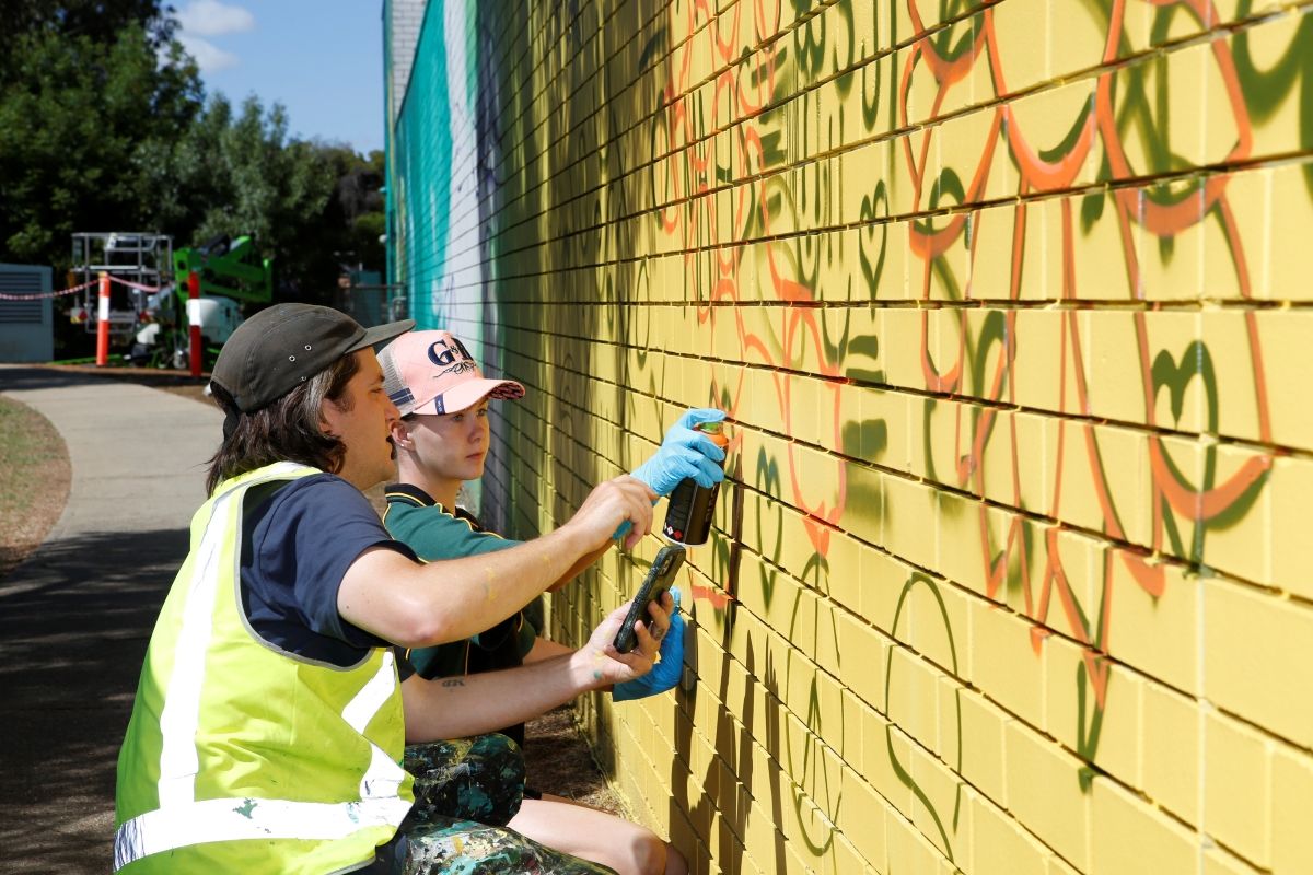 Artist helping student paint on the wall.