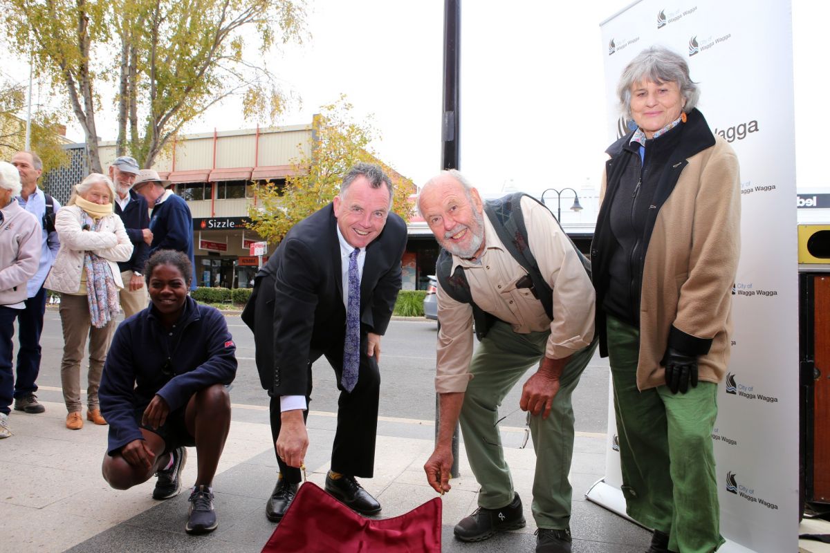 Two men unveiling plaque, watched by two women