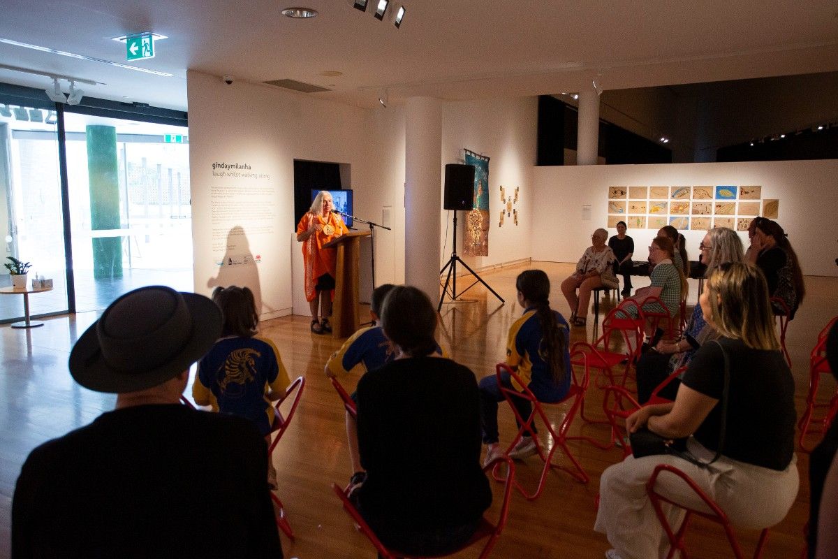 A group of people watch as a woman speaks on a microphone