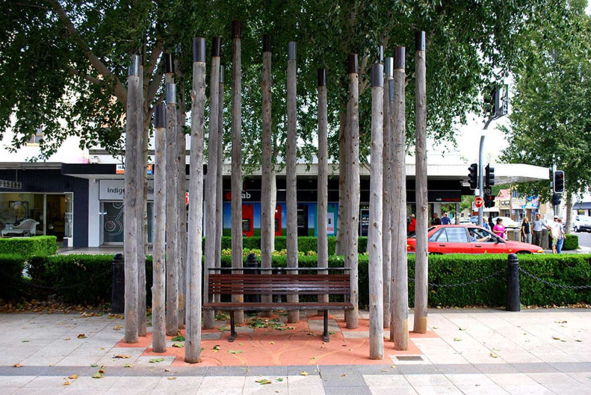A public seat surrounded by tall wooden poles. 