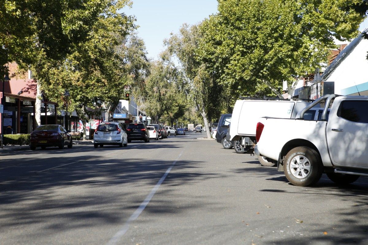 View of a main street in the CBD, line with trees and parked cars, with vehicle driving up the street in the background.