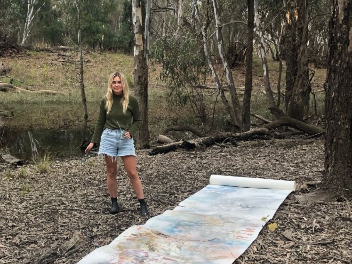 Woman standing in bushland with artwork laid out on ground