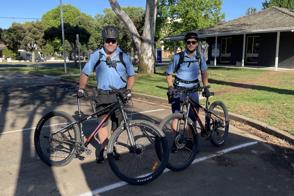 Two police officers standing with their police bicycles in a public carpark. 