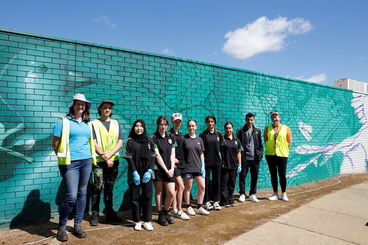 Group of students and adults standing next to a mural.