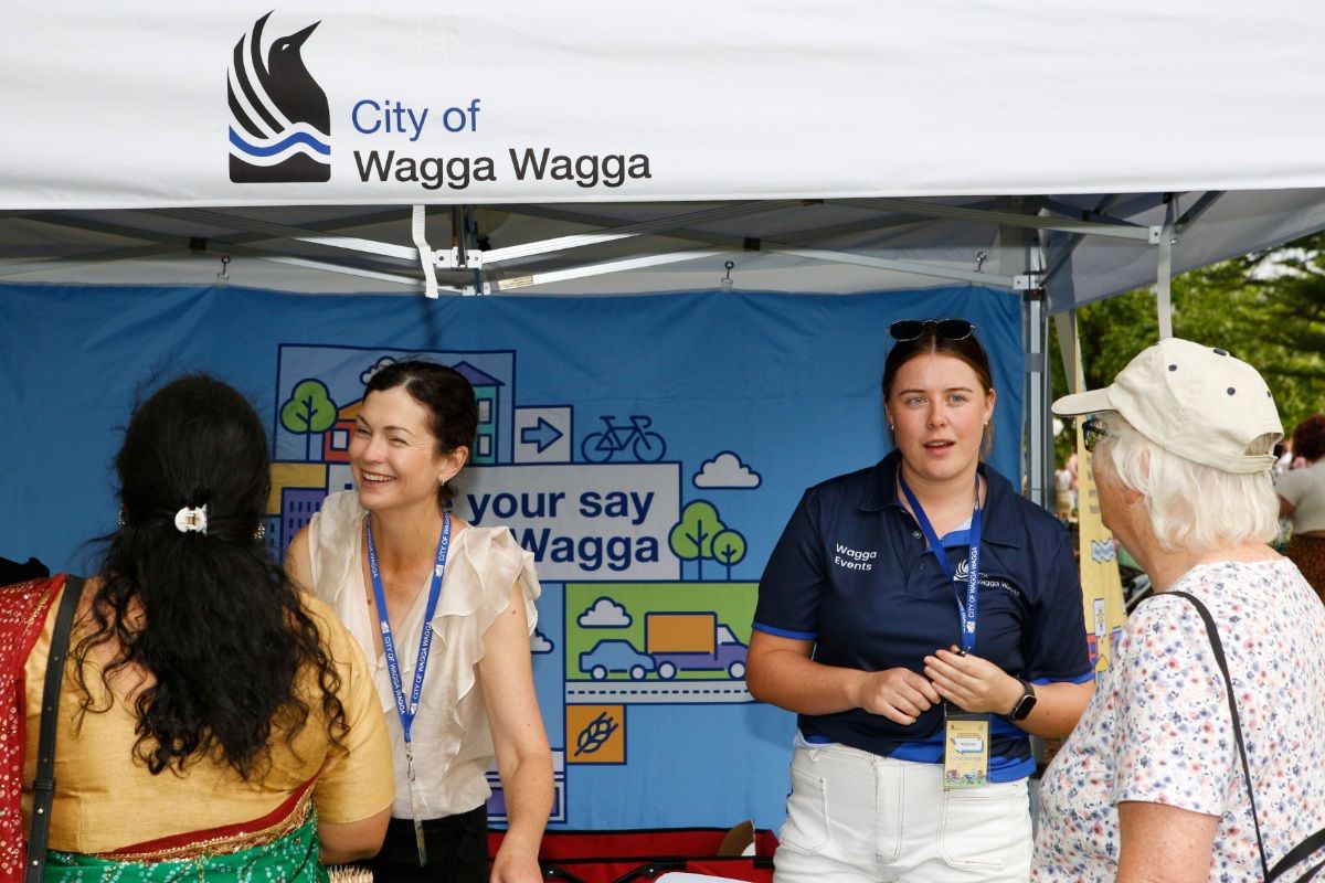 Front view of two women standing under marquee and talking to two other women.