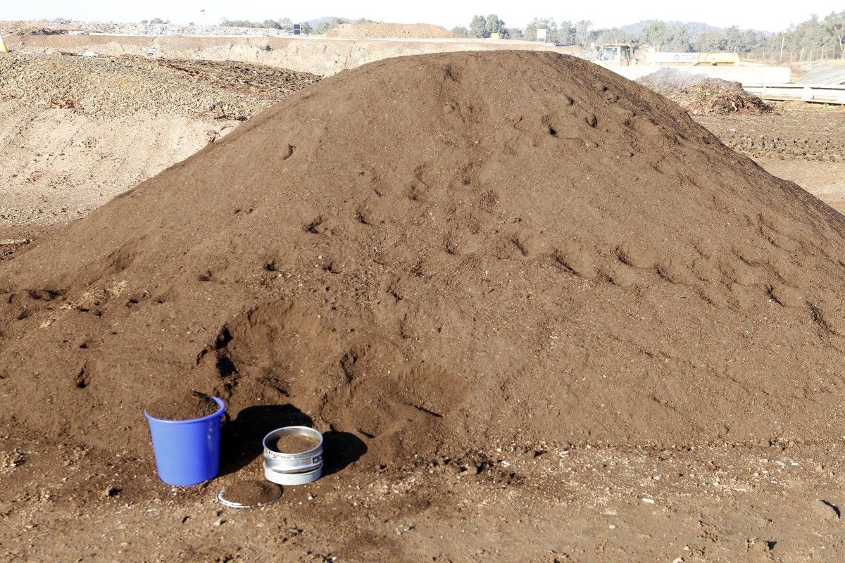 A pile of compost, with two buckets resting again the front of the pile.