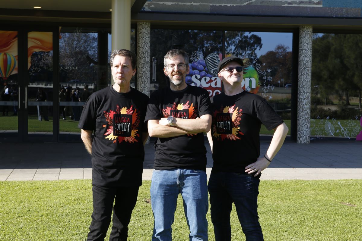 three men standing in front of the Wagga Civic Theatre wearing Wagga Comedy Fest shirts.