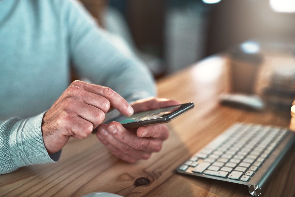 Hands holding mobile phone with laptop on desk