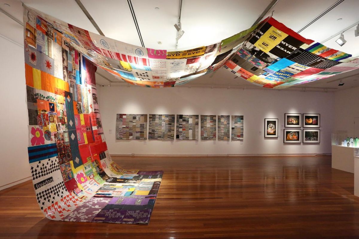 A large quilt made from plastic bags hangs in a gallery space