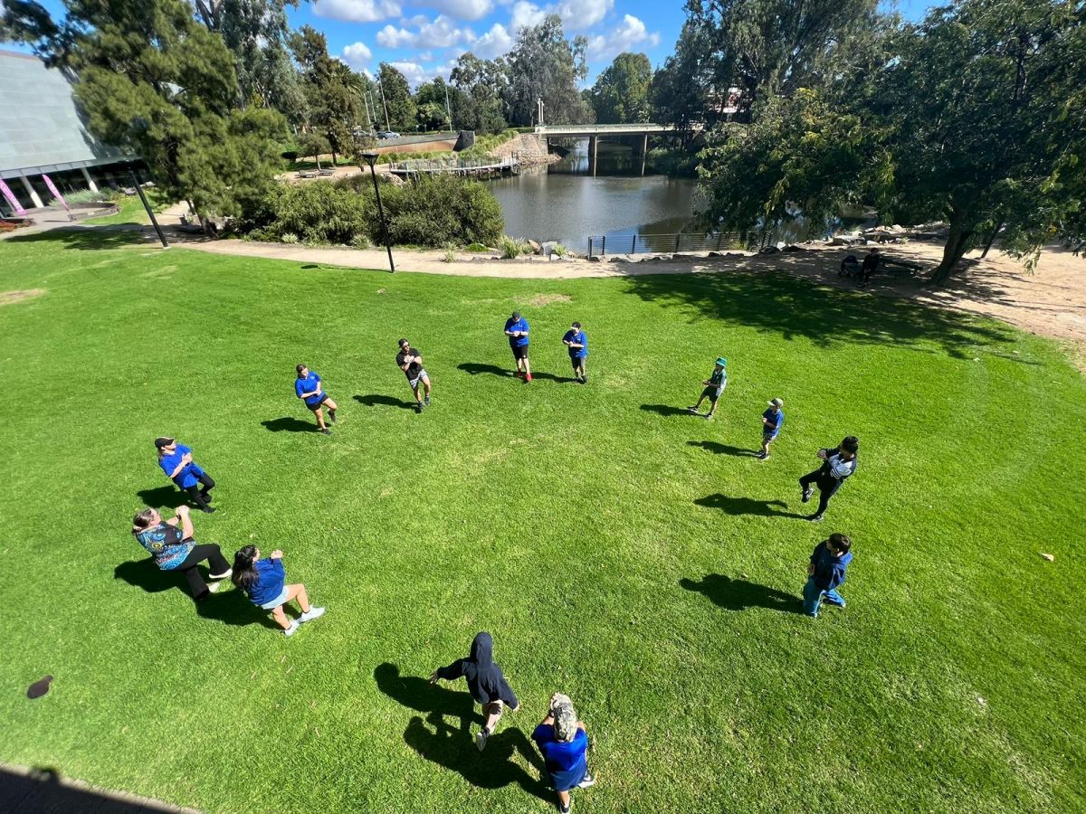 Top view of students in circle on lawn in front of Civic Theatre, with Wollundry Lagoon in background