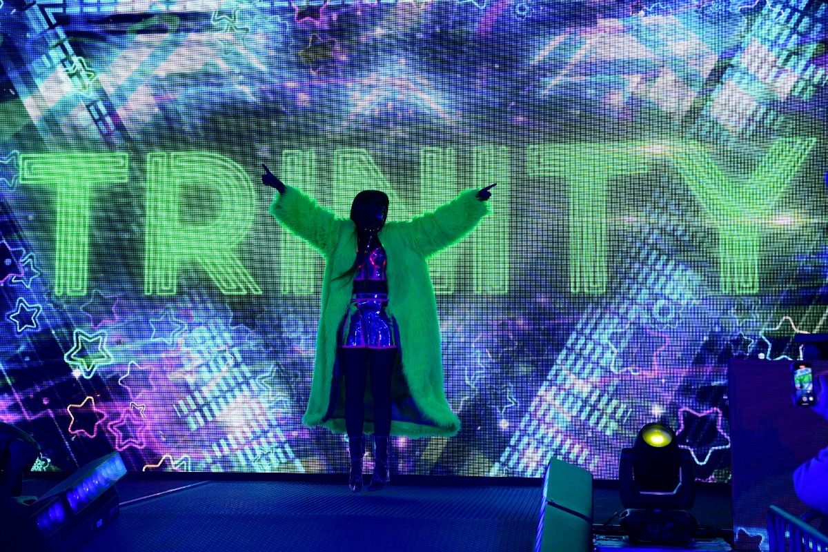 Female wrestler on stage in front of screen with Trinity on it