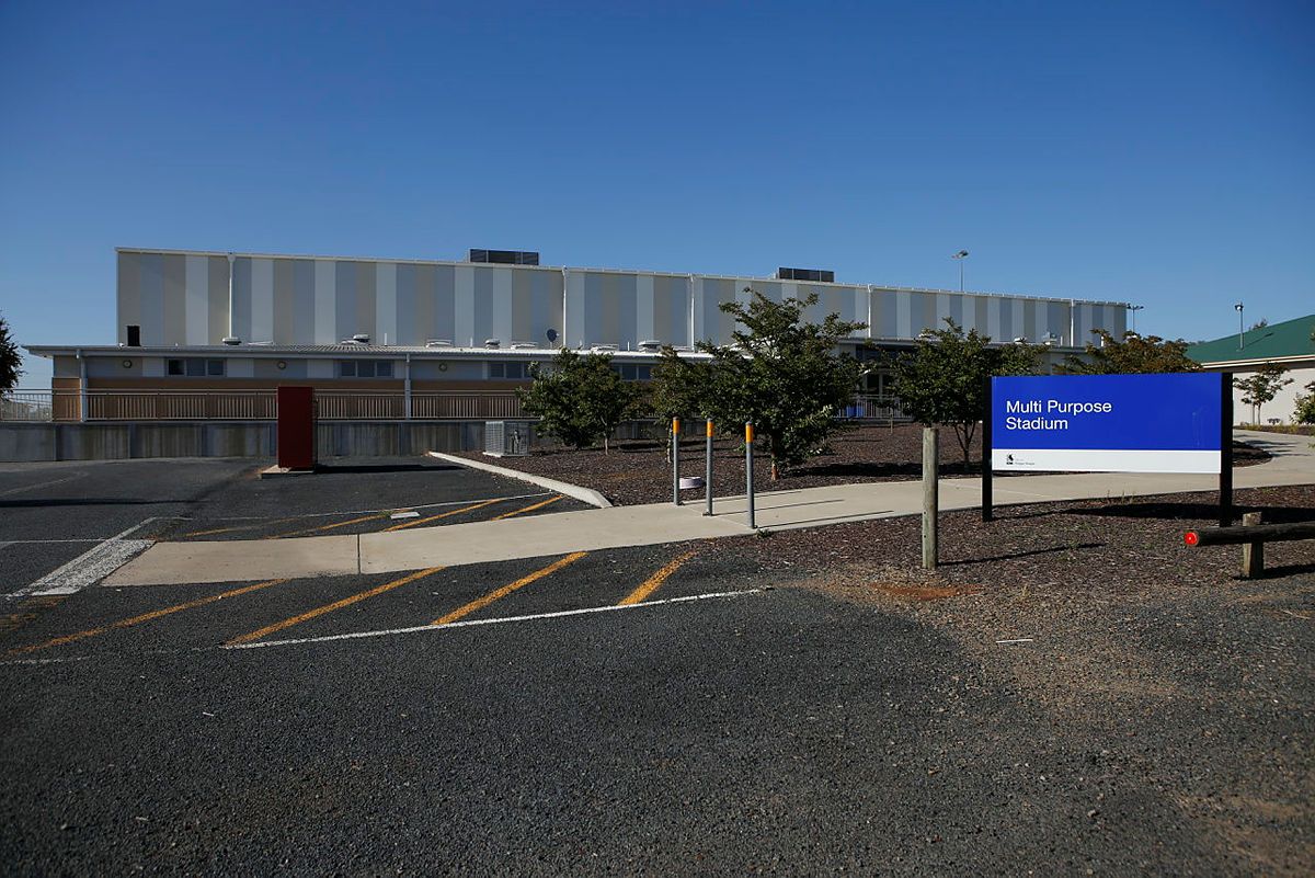 The facade of a large modern building on a sunny day. There is a blue sign in front of the building that says 