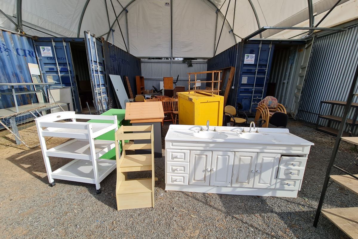 Some unwanted furniture sits in a second-hand yard under a temporary shelter.