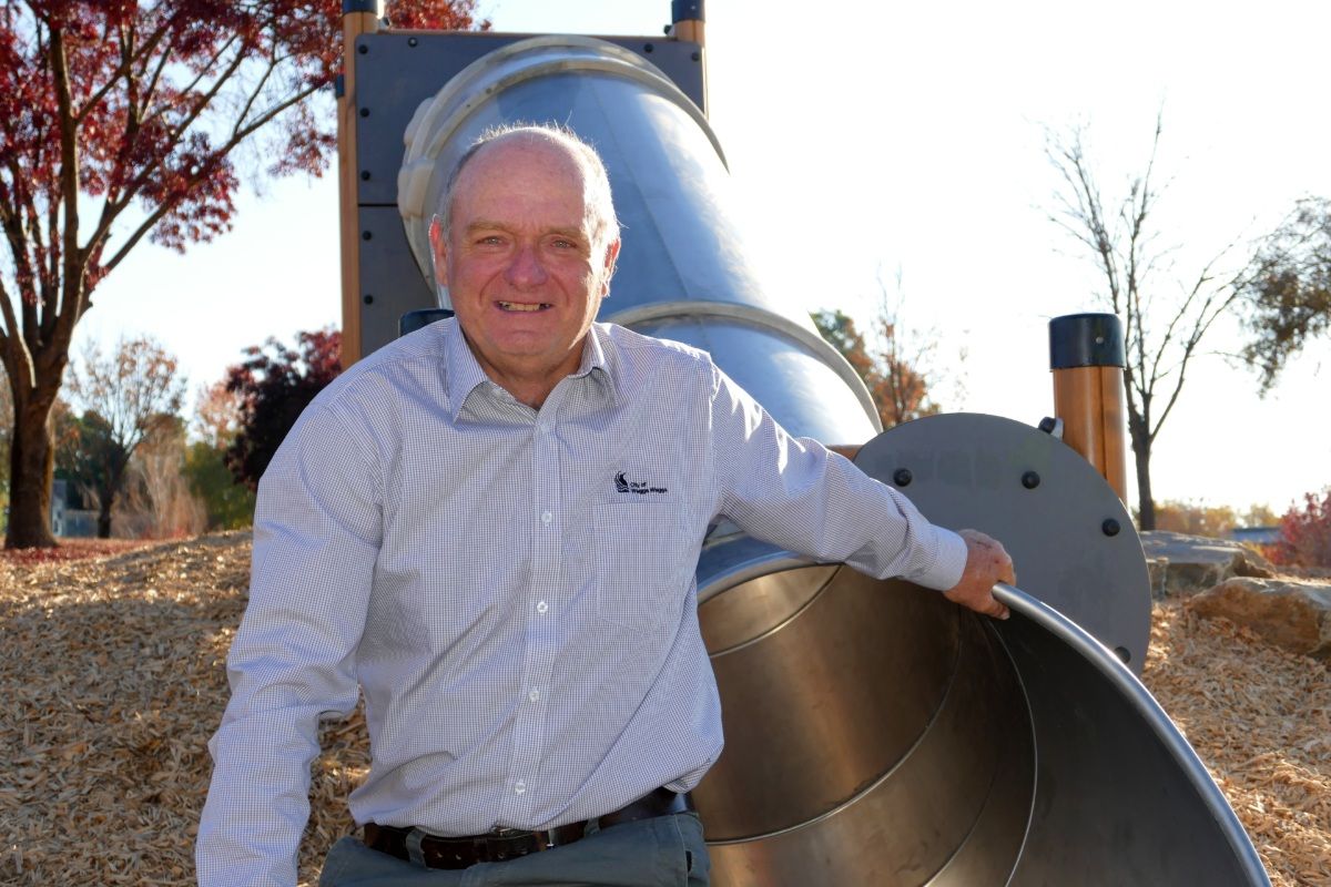 Man sitting on side of large steel slide, smiling at camera.