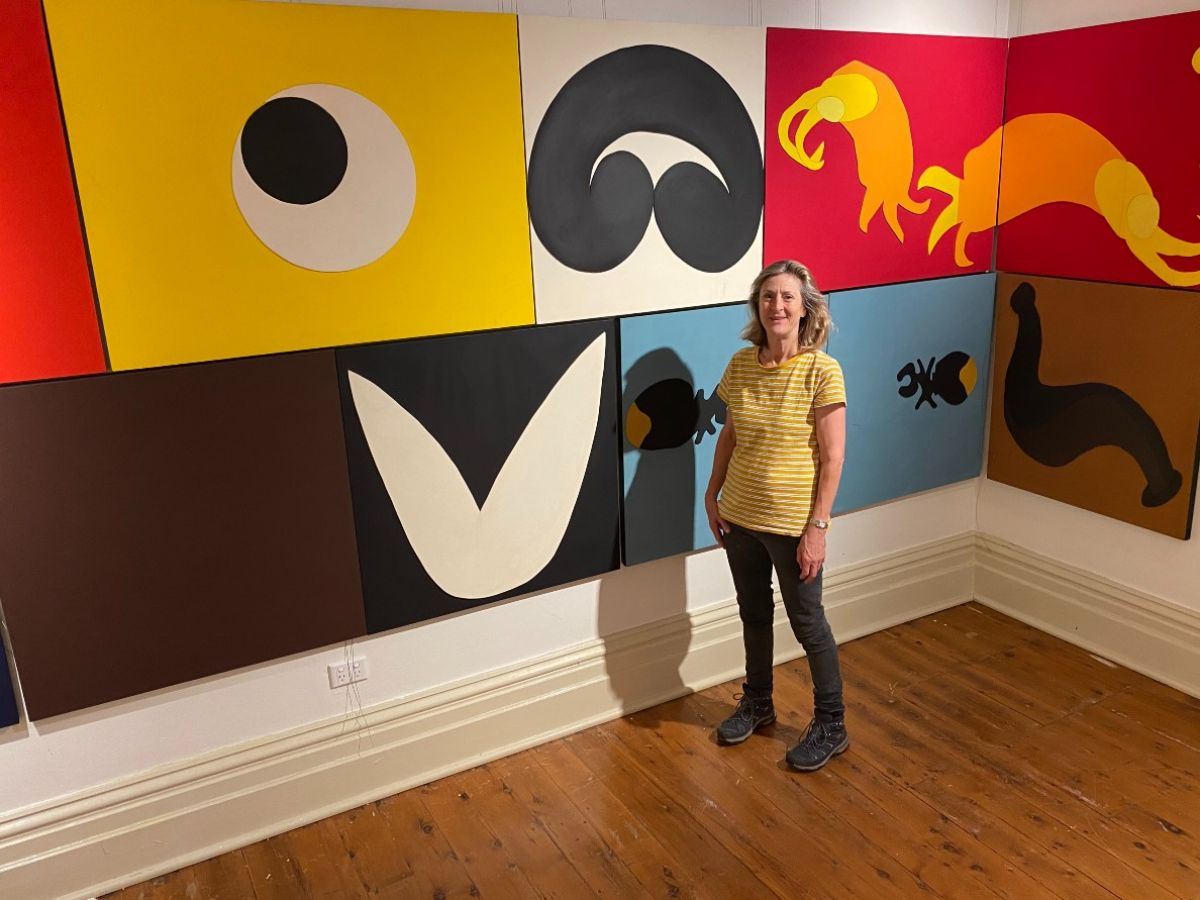 A woman stands in front of a series of artworks