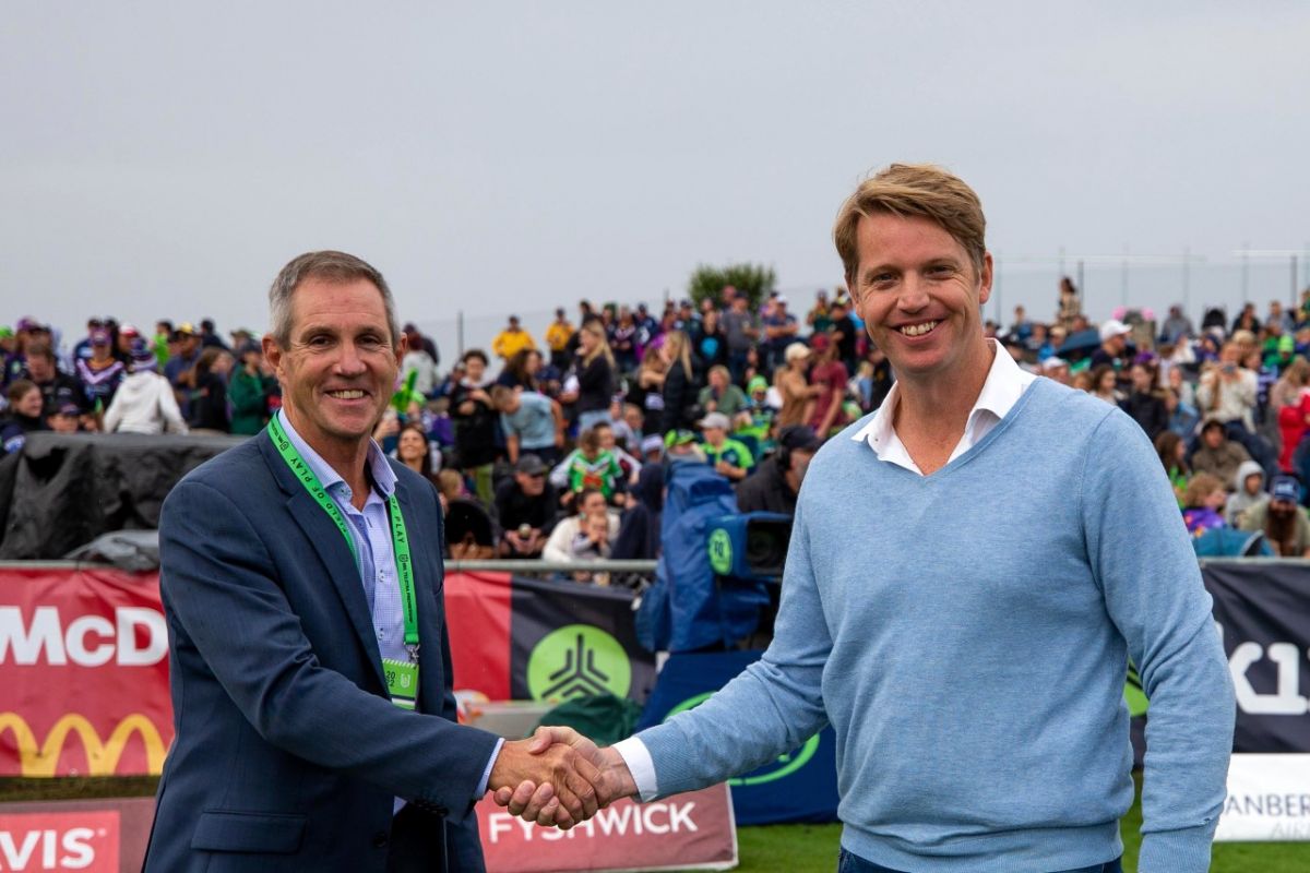 Two men shaking hands with crowd in background