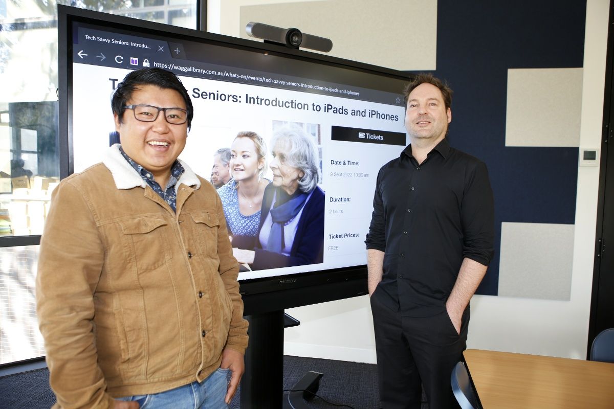 Two men standing in front of large tv screen with Tech Savvy information