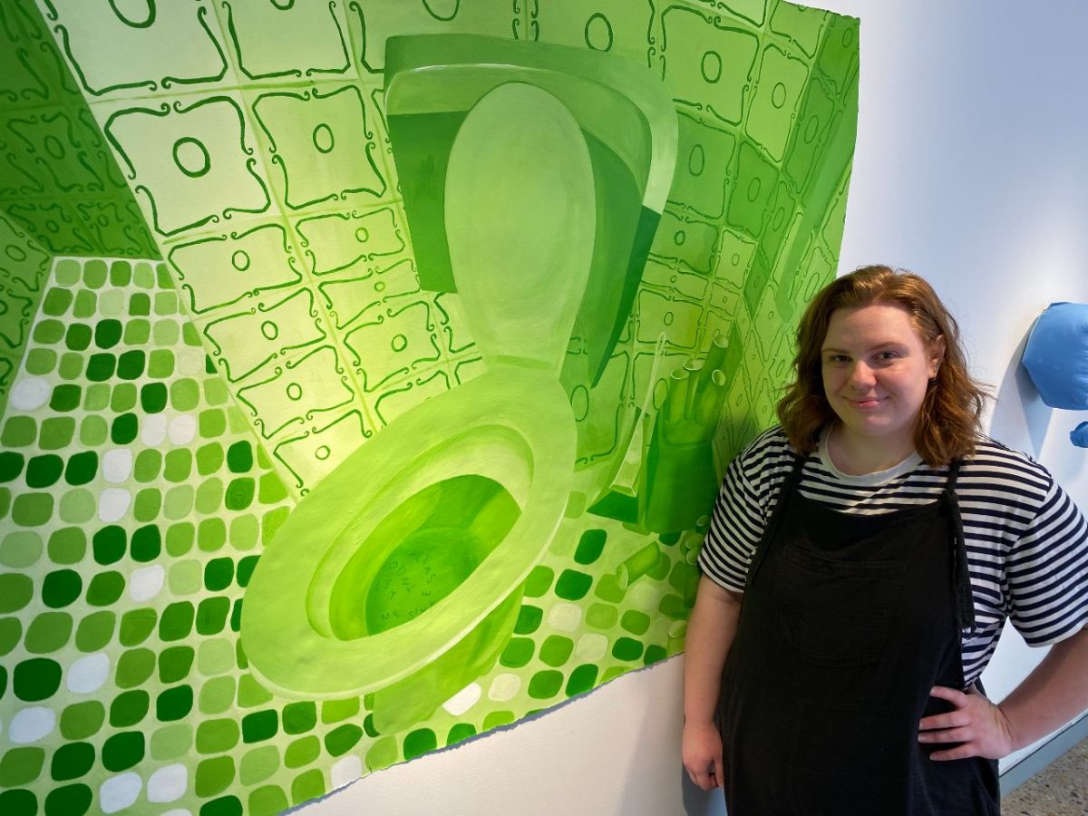 A young woman stands beside a green artwork